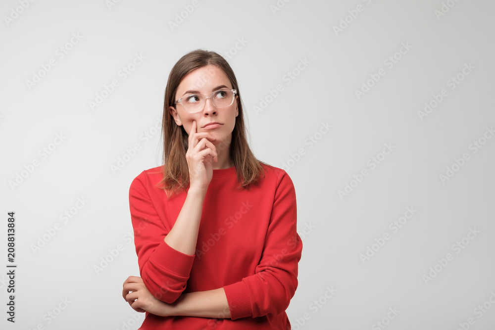 thoughtful european woman in red sweater is looking up thinking or planning. Concept of doubtful mind - obrazy, fototapety, plakaty 