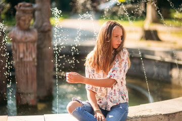 Wall Mural - blond teenage girl in a blond blouse playing with her hair on the background of a fountain