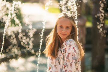 Wall Mural - blond teenage girl in a blond blouse playing with her hair on the background of a fountain