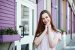 © Мария Балчугова - human emotion. portrait of a young cheerful girl with long hair on the background of a beautiful lilac facade of the house or cafe. the model smiles cheerfully and cheerfully looks at the camera