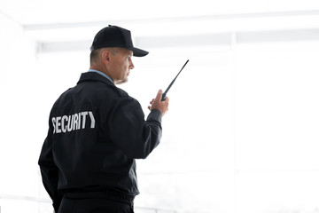 Wall Mural - Male security guard using portable radio transmitter on light background