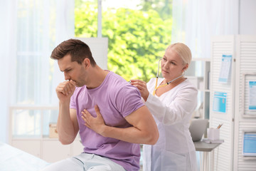 Canvas Print - Doctor examining coughing young man at clinic