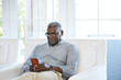 © trinettereed/Stocksy - African American Senior man texting on a smart phone sitting on the couch at home