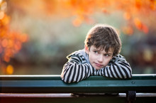 Boy In A Thoughtful Position On A Park Bench In Autumn