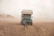 Woman Carrying Sand Ladders To A Camping Truck In The Desert During Heavy Sand Storm