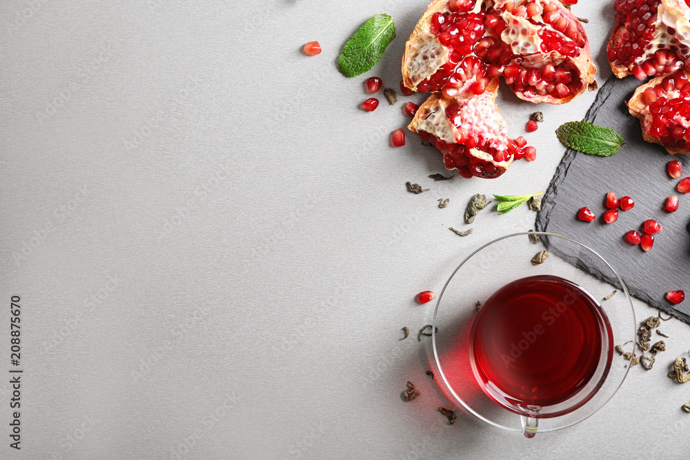 Flat lay composition with glass cup of red tea and pomegranate on grey background