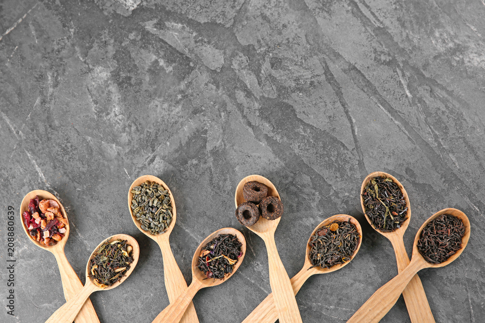 Different sorts of tea in spoons on grey textured background, flat lay