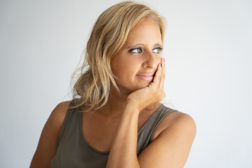 Wall Mural - Closeup of pensive blonde lady in casual sleeveless shirt looking aside. Beautiful Caucasian woman leaning chin on hand, thinking and smiling. Reflecting concept