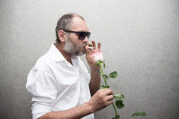 brutal man in glasses with a beard and a cigarette lights a rose