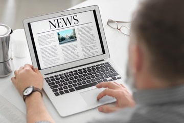 Senior man reading news on laptop screen at home