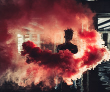 Young African Man Stands Under Bridge And Holds Colored Red Smoke Bomb In His Hands.