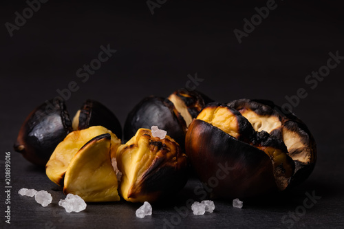 Fotografie, Obraz Closeup of roasted chestnuts with grains of salt on a black background