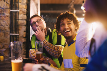 Cheerful soccer fans have gathered in a local pub to drink beer and discuss upcoming games.