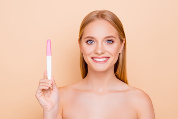 Wall Mural - Portrait of attractive joyful cheerful charming pretty glad woman demonstrating positive result on pink and white intimate test stick isolated on beige background looking at camera