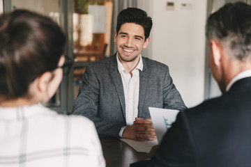 Poster - Business, career and placement concept - young caucasian man smiling, while sitting in front of directors during corporate meeting or job interview