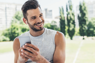 Wall Mural - close-up portrait of handsome young man listening music with smartphone and earphones outdoors