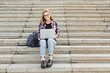 © Prostock-studio - Smiling student sitting on stairs using laptop