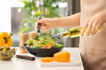 Woman dressing fresh vegetable salad with olive oil in kitchen