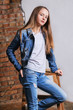 Fashion portrait beautiful young woman, girl wearing blank white cotton T-shirt, denim jacket and jeans.Young female teenager model posing, standing by chair, hand in pocket pants. model tests.