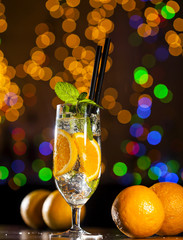 Wall Mural - Fresh cocktail with orange, ice ang mint leaves on bar lights background