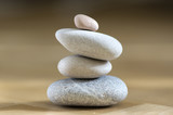 Fototapeta Desenie - Group of zen stones pile, grey meditation pebbles tower on light brown wooden background in sunlight