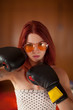 pretty young woman with red hair, sunglasses and boxing gloves looks upset, feminism, self defense concept 