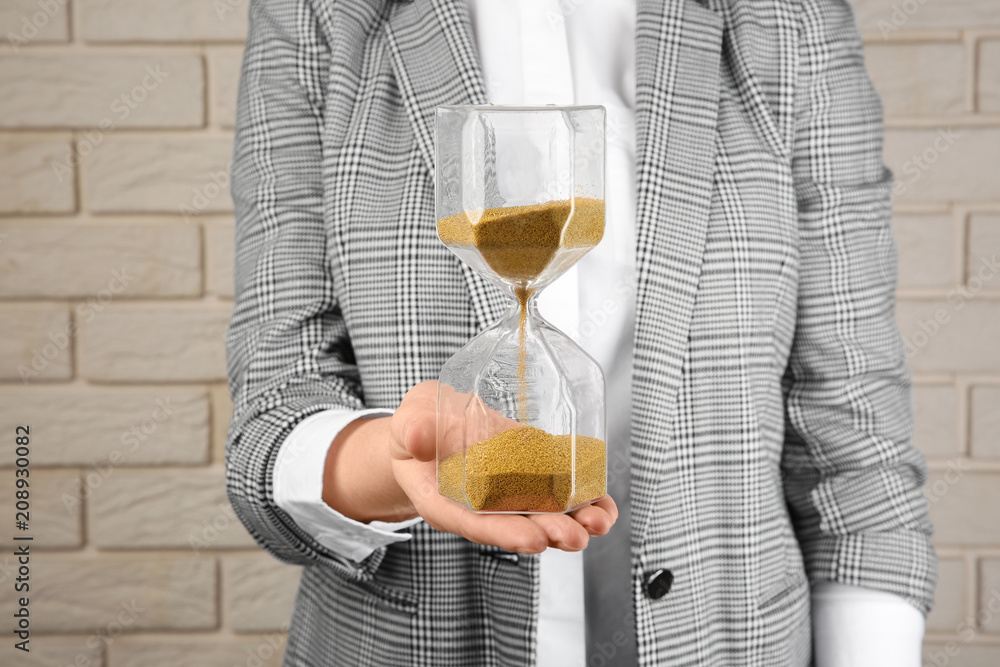 Woman holding hourglass near brick wall. Time management concept