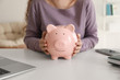 © Pixel-Shot - Young woman holding piggy bank indoors, closeup. Money savings concept
