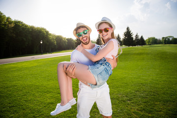 Poster - Portrait of positive playful couple in casual outfits outside enjoying beautiful landscape, handsome strong man holding redhead lover. Pleasure delight recreation harmony