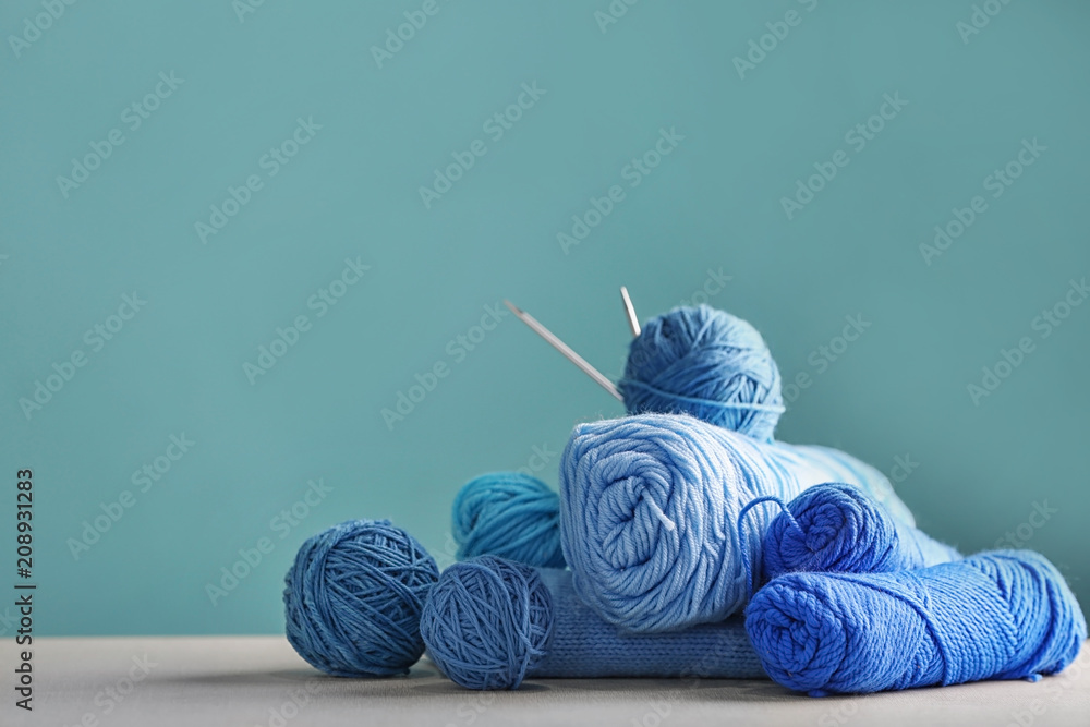 Knitting yarn with needles on table against color background