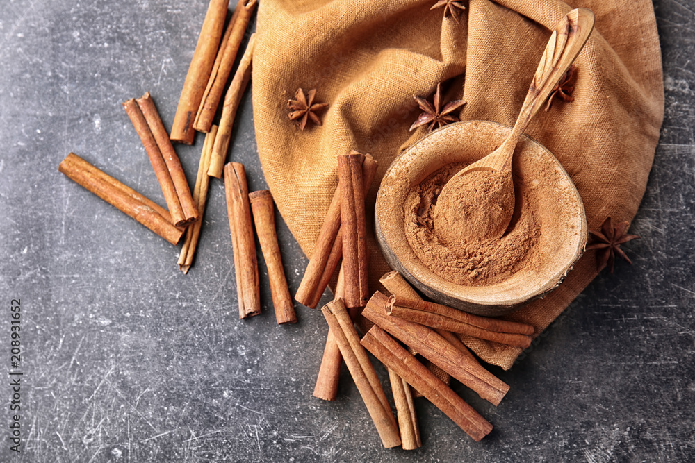 Composition with cinnamon powder and sticks on grey background