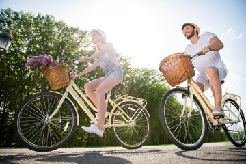 Poster - Portrait of sportive brother and sister riding retro bikes with baskets and flowers, enjoying beautiful nature. Landscape sun sunlight sunny day healthy lifestyle fitness people concept