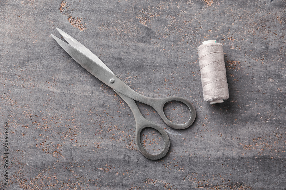 Sewing thread and scissors on grey background