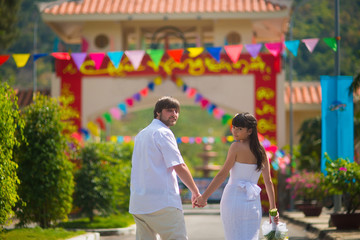 The bride and groom look at the camera, leaving the summer Park outdoors, holding hands