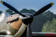 A Photograph Documenting The Propeller And Shroud Covering The Cockpit Of An RAF Hawker Hurricane As Stands On An Airstrip Under Blue Skies Waiting To Be Flown.