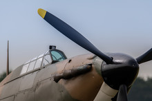 A Photograph Documenting The Propeller And Cockpit Glass Of An RAF Hawker Hurricane As Stands On An Airstrip Under Grey Skies Waiting To Be Flown.