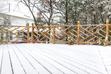 Empty wooden deck of house with statue decorations on backyard in neighborhood with snow covered wood floor during blizzard white storm, snowflakes falling in Virginia suburb