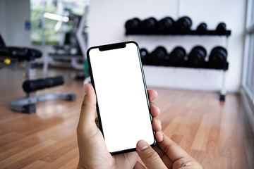 Wall Mural - young man hand holding smartphone in gym to fitness phone fitness exercise concept
