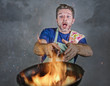 © TheVisualsYouNeed - shocked messy man with apron holding pan in fire burning the food in kitchen disaster and unskilled and unexperienced terrible home cook