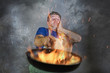 © TheVisualsYouNeed - shocked messy man with apron holding pan in fire burning the food in kitchen disaster and unskilled and unexperienced terrible home cook