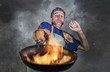 © TheVisualsYouNeed - shocked messy man with apron holding pan in fire burning the food in kitchen disaster and unskilled and unexperienced terrible home cook
