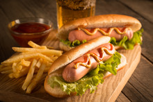 Photo Of Barbecue Grilled Hot Dog With Yellow Mustard And Ketchup On Wooden Background. Hot Dog Sandwich With Potato Fries And Sauces.