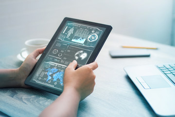 Hands of woman using tablet on wooden table with HUD user interface for cyber futuristic technology concept