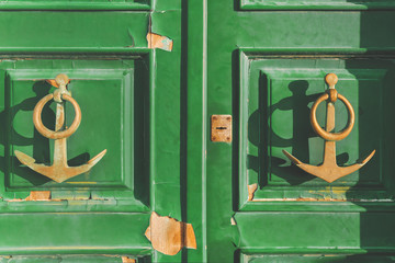 Wall Mural - Old green wooden door with two door knocker in the shape of an anchor