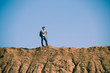 © snedorez - Picture of afar of tourist man with sticks for walking on hill against blue sky