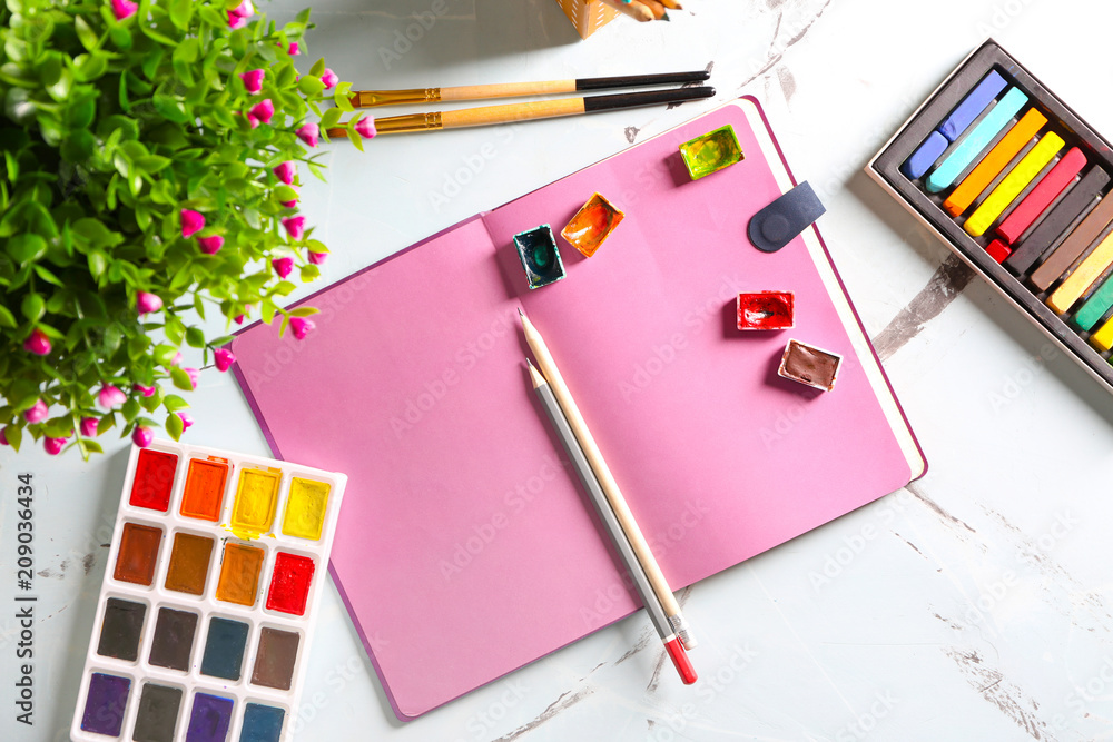 Notebook with paints and pencils of professional artist on table