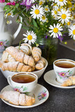 Fototapeta Tulipany - Croissants (bagels) with poppy seeds and tea on a bouquet of flowers field background. Morning tea with croissants.
