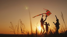 Happy Family Playing With A Kite At Sunset. Mom, Dad And Daughter Are Happy Together