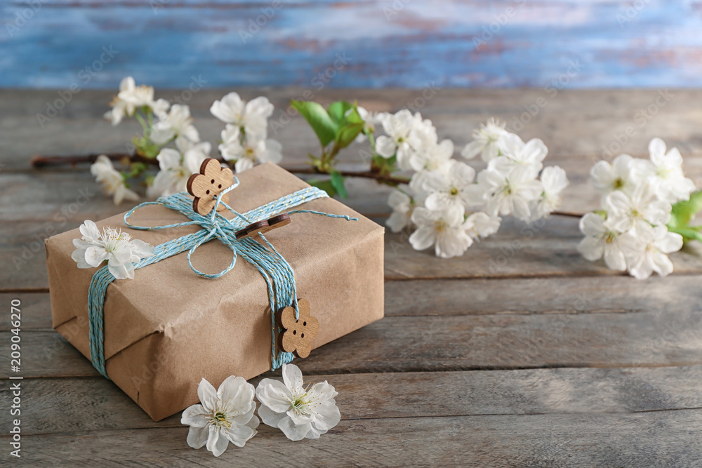 Stylish gift box and blossoming branch on wooden background