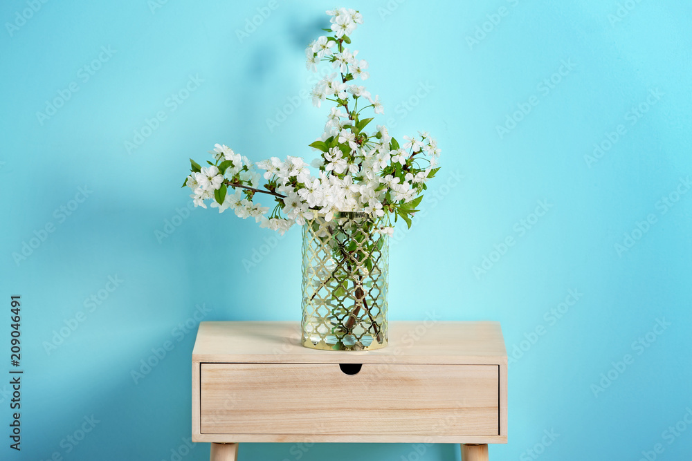 Vase with beautiful blossoming branches on table against color background